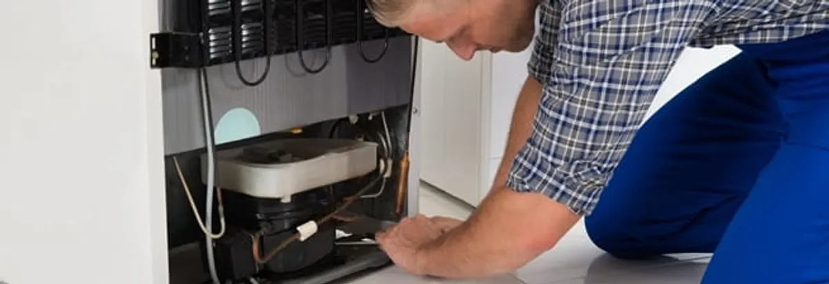 Refrigerator repair technician servicing the compressor and condenser area in Madison, WI